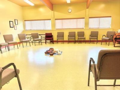group room with many grey chairs sitting in a circle with a couple dark red chairs for elders