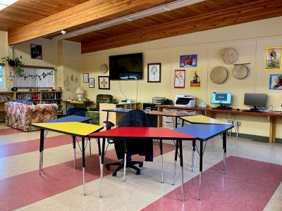 learning centre with drums on the wall, a tv, and tables that form a circle surrounding a teachers chair